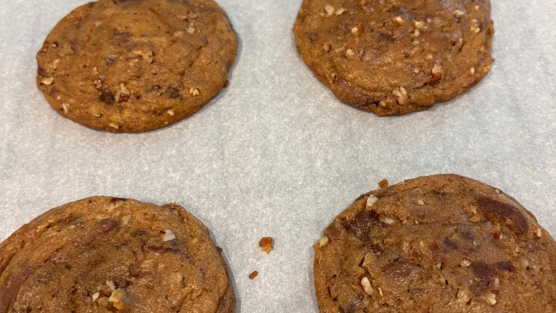 Freshly baked Unshaken brown butter chocolate chip pecan cookies cooling on parchment paper