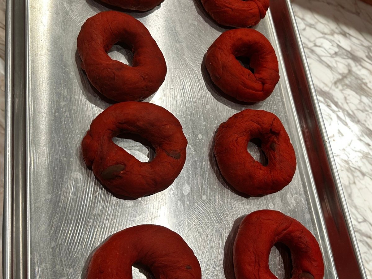 Hand-rolled red velvet bagels resting on a baking sheet before baking